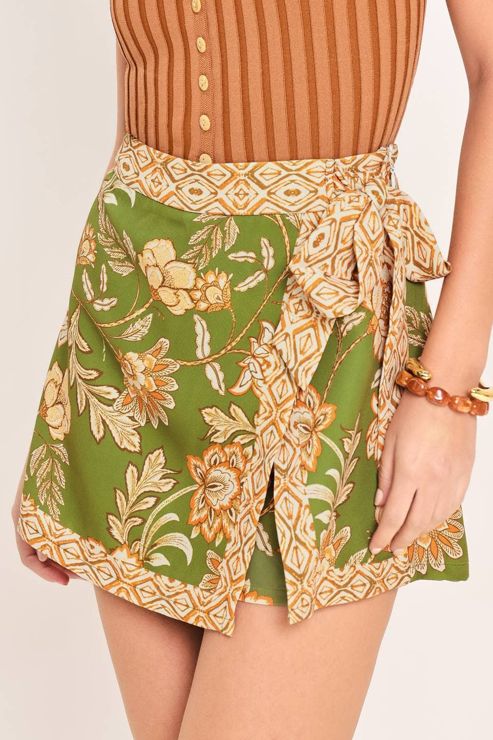 Woman wearing a brown sleeveless top and green floral skirt on a white background