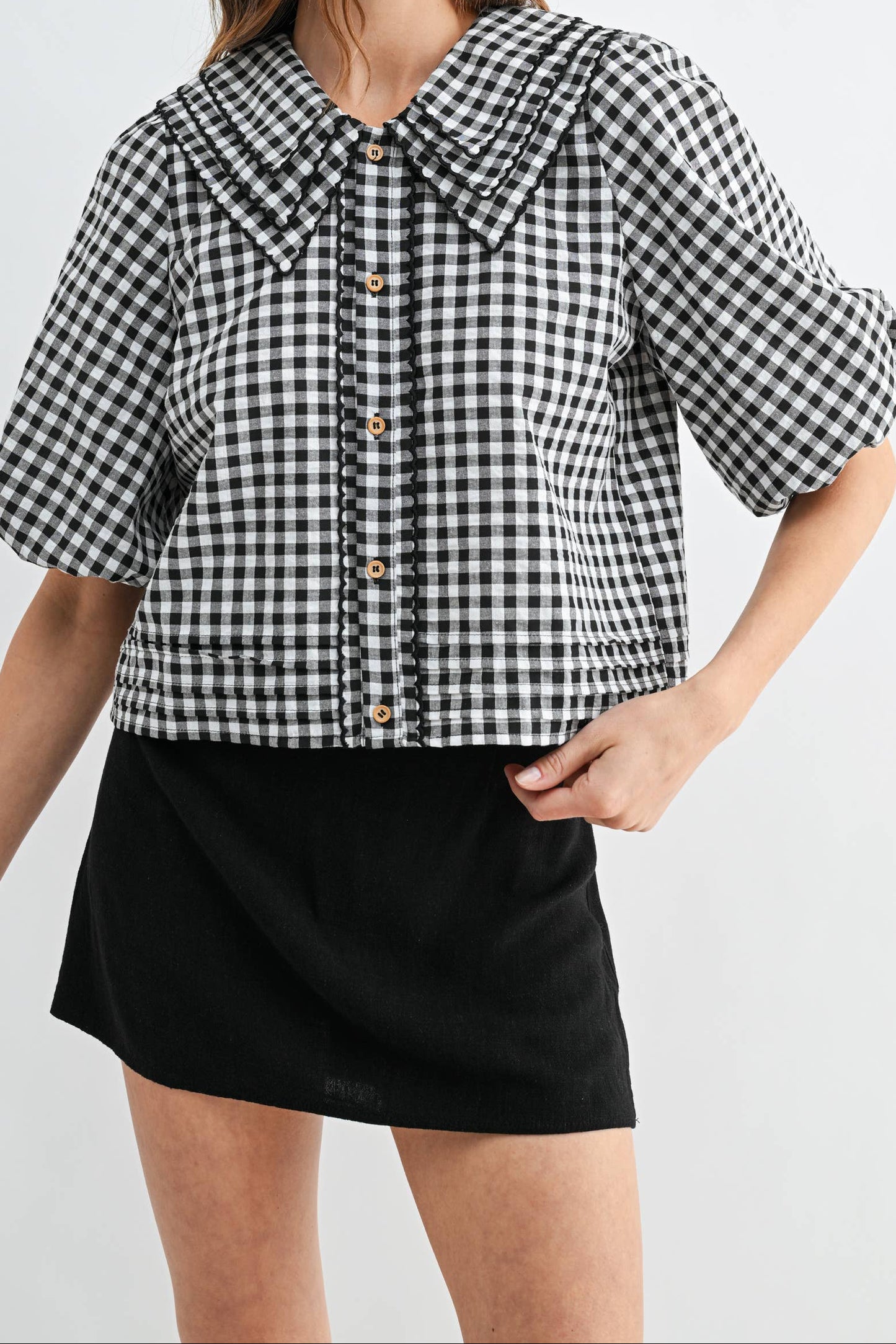 Woman wearing a black and white checkered blouse with a collar on a white background