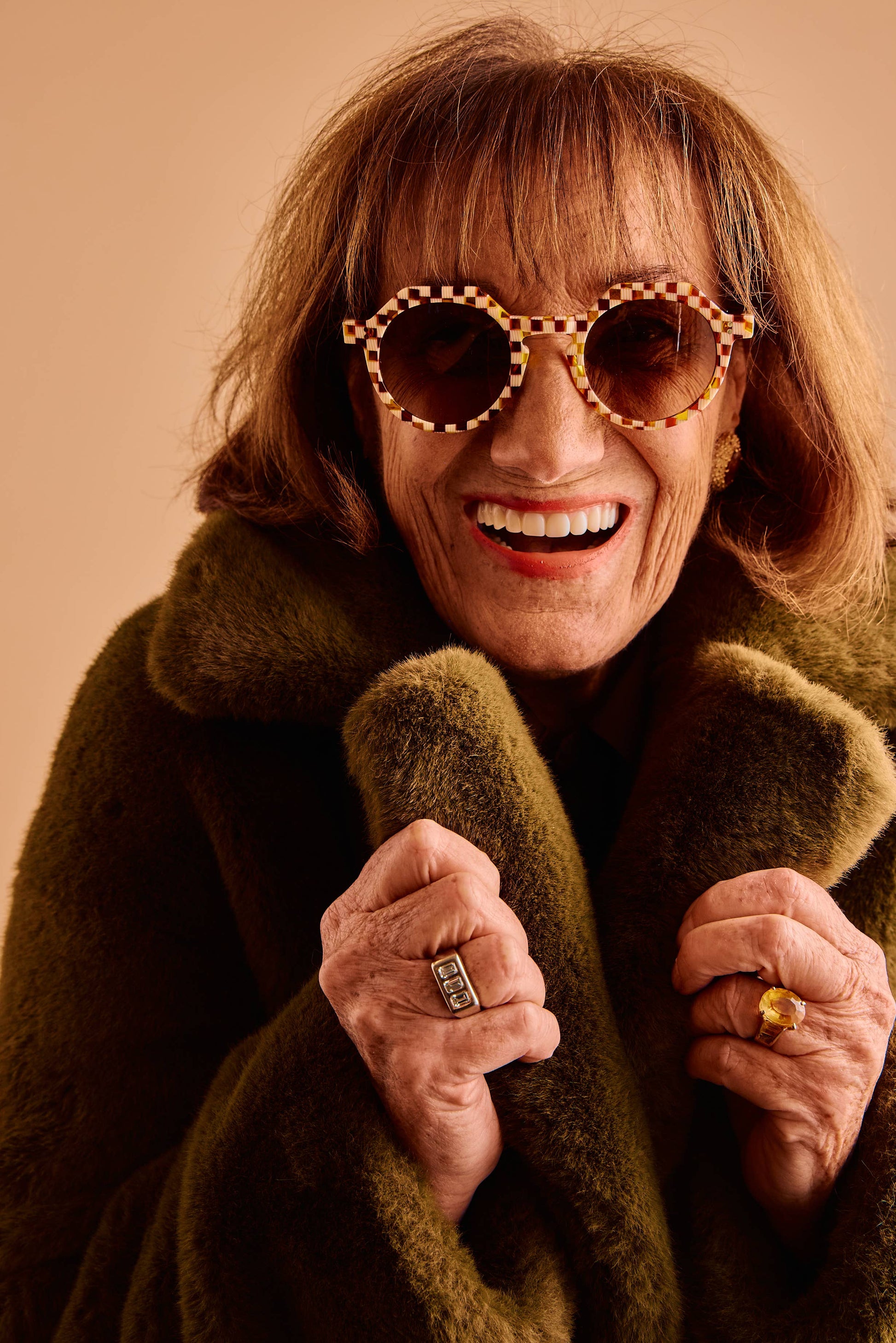 Person wearing a green coat and sunglasses with a beige background