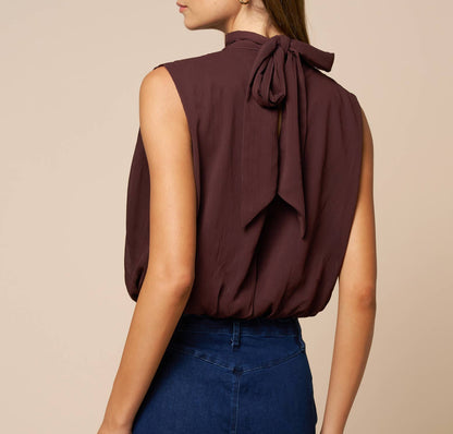 Woman wearing a brown sleeveless top with a bow detail on a beige background