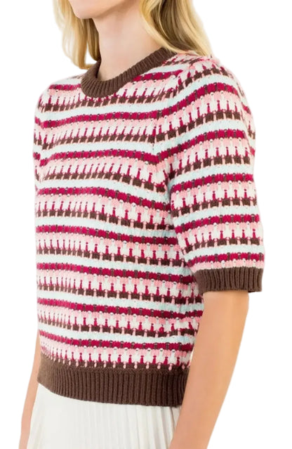 A woman wearing a short-sleeve knit sweater with horizontal stripes in brown, magenta, and white, featuring a ribbed crew neck, cuffs, and hem. A small 'PLUS' label is visible in the top right corner.
