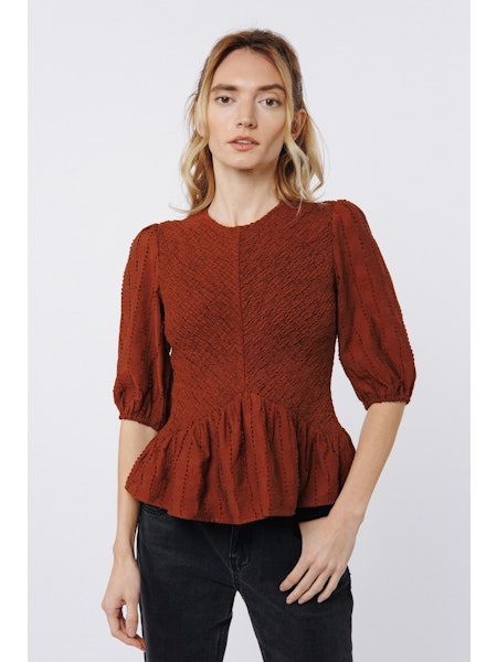 Woman wearing a rust-colored textured blouse with puffed sleeves on a white background