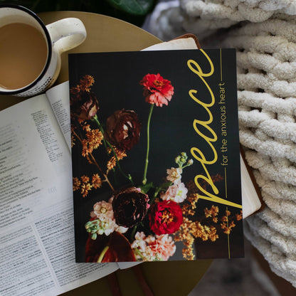 Book with a floral cover titled 'Peace for the Anxious Heart' next to a cup of coffee on a textured surface.