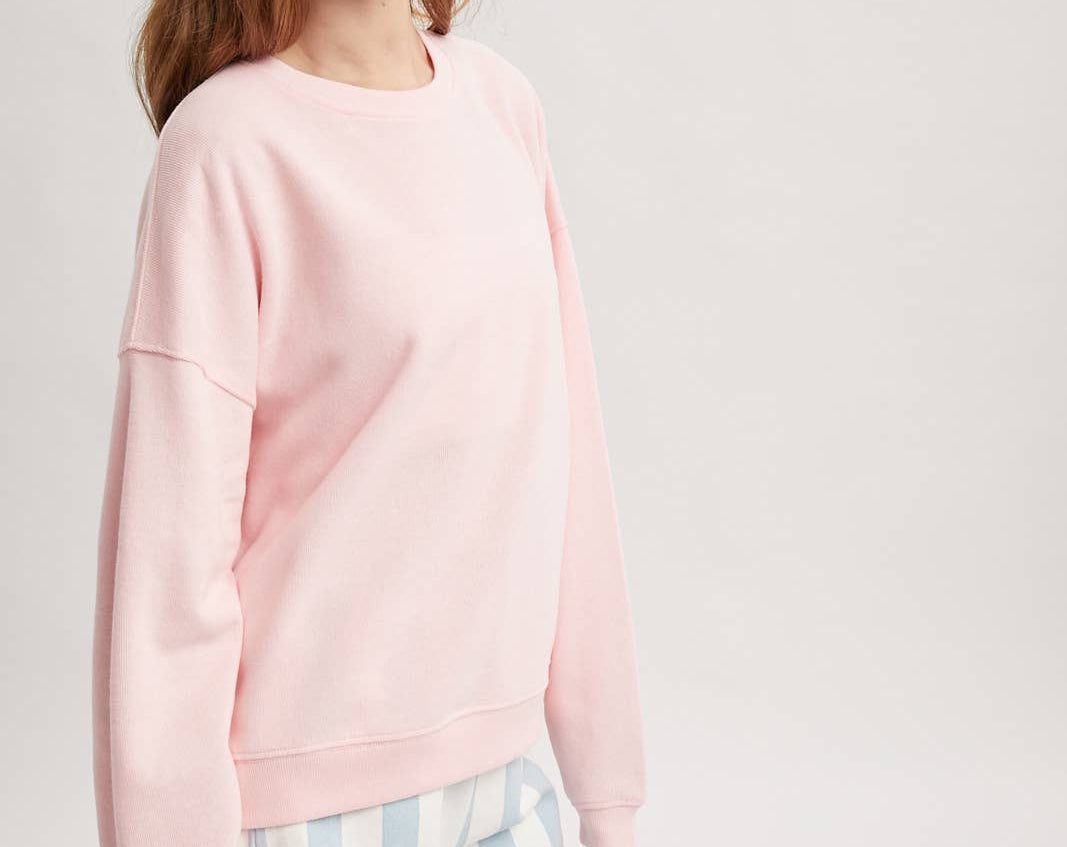 Woman wearing a pink sweatshirt and striped shorts on a white background