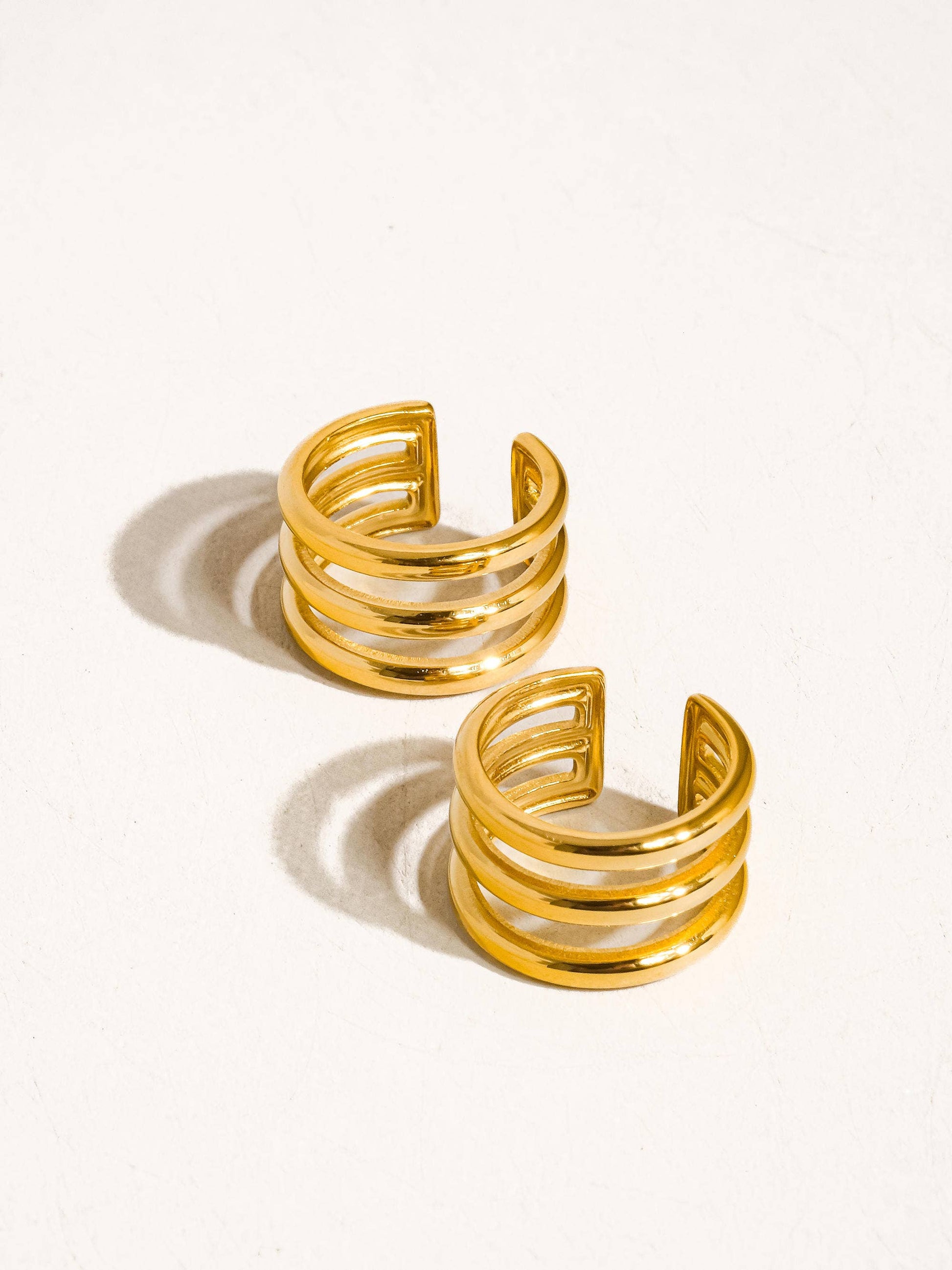 Pair of gold open cuff earrings on a white background