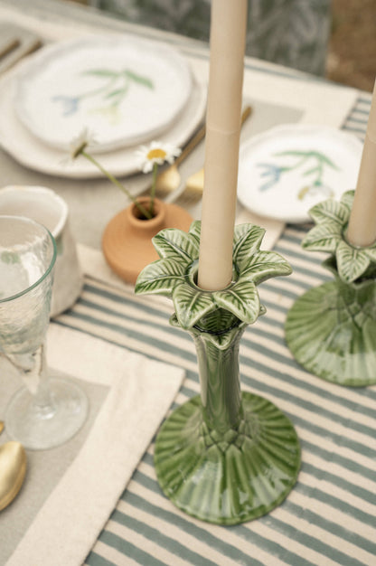 Green ceramic candle holder with a white candle on a table setting.