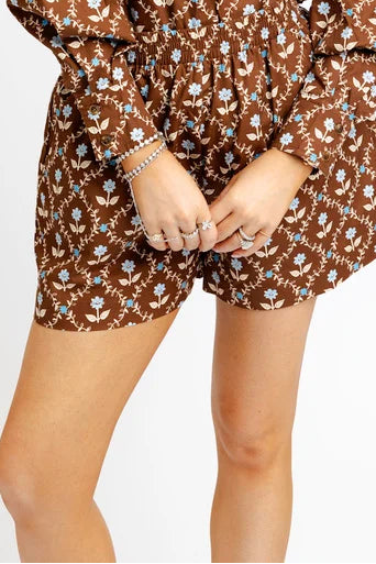 A woman wearing brown and blue floral shorts standing  against a plain white studio background.