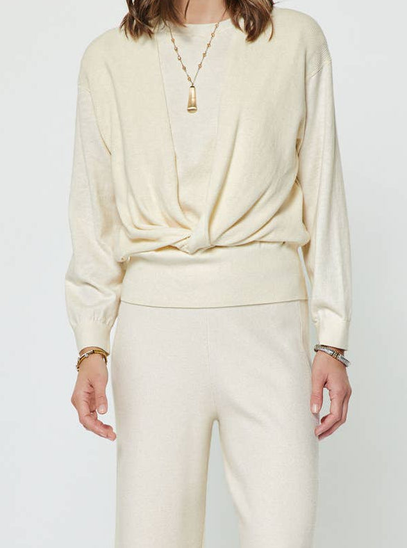 A woman wearing a cream sweater with a twist in the front. 