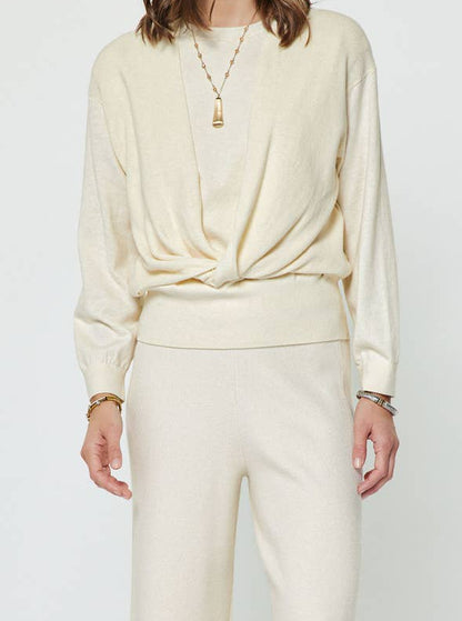 A woman wearing a cream sweater with a twist in the front. 
