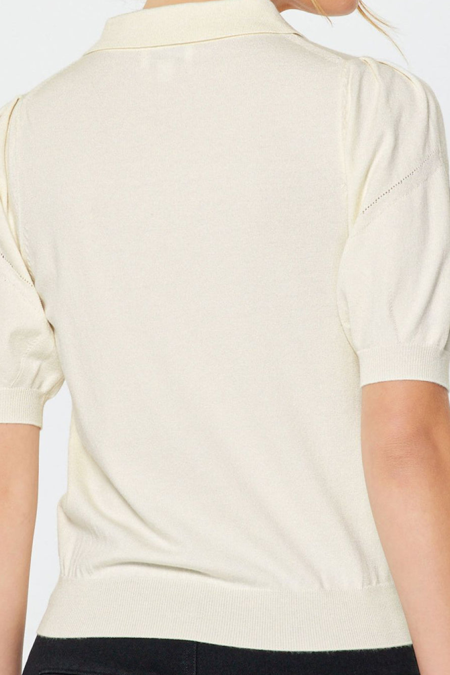 Woman wearing a white polo shirt and black pants on a plain background