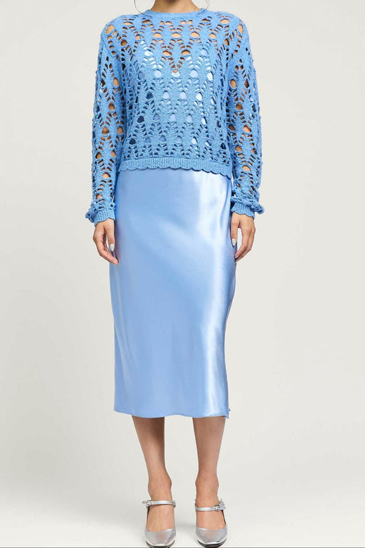 Woman wearing a blue lace top and light blue skirt on a white background