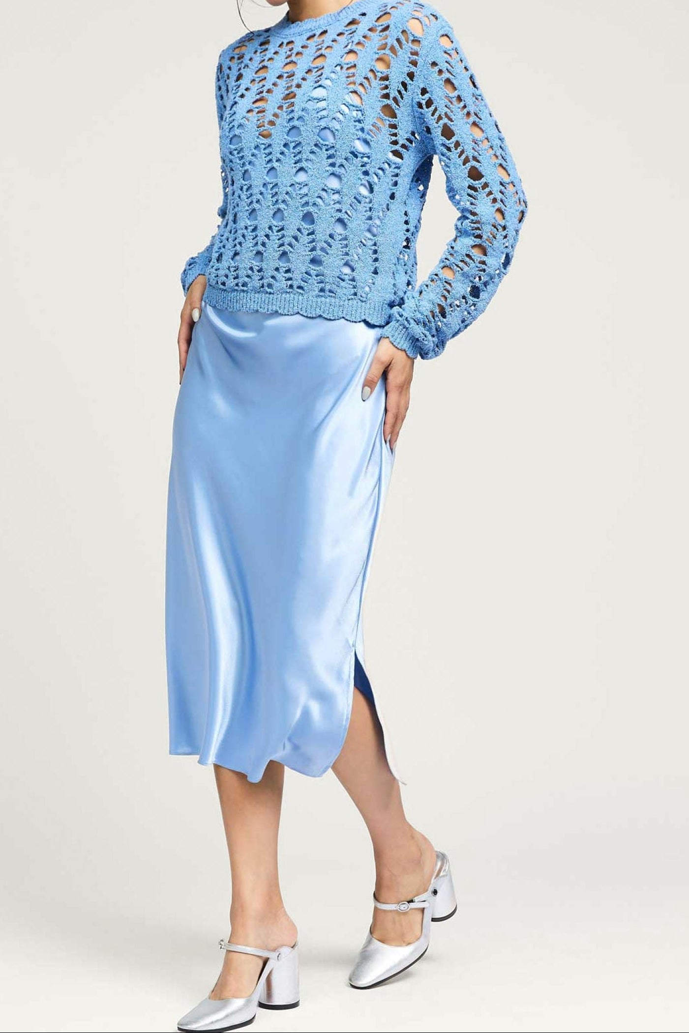 Woman wearing a light blue lace top and satin skirt on a white background