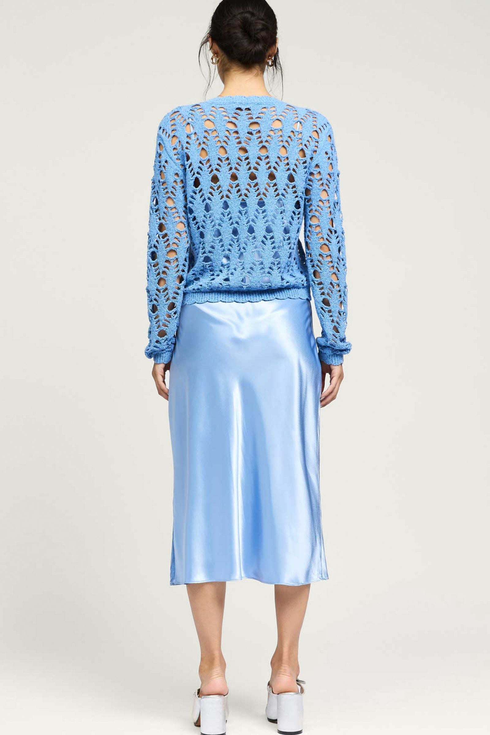 Woman wearing a blue lace top and satin skirt on a white background