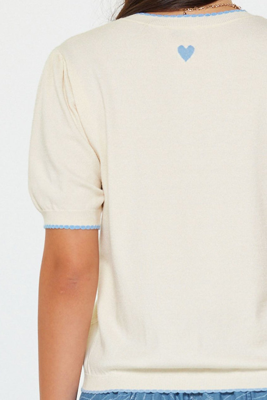 Person wearing a cream-colored sweater with a blue heart design on the back, standing against a white background.