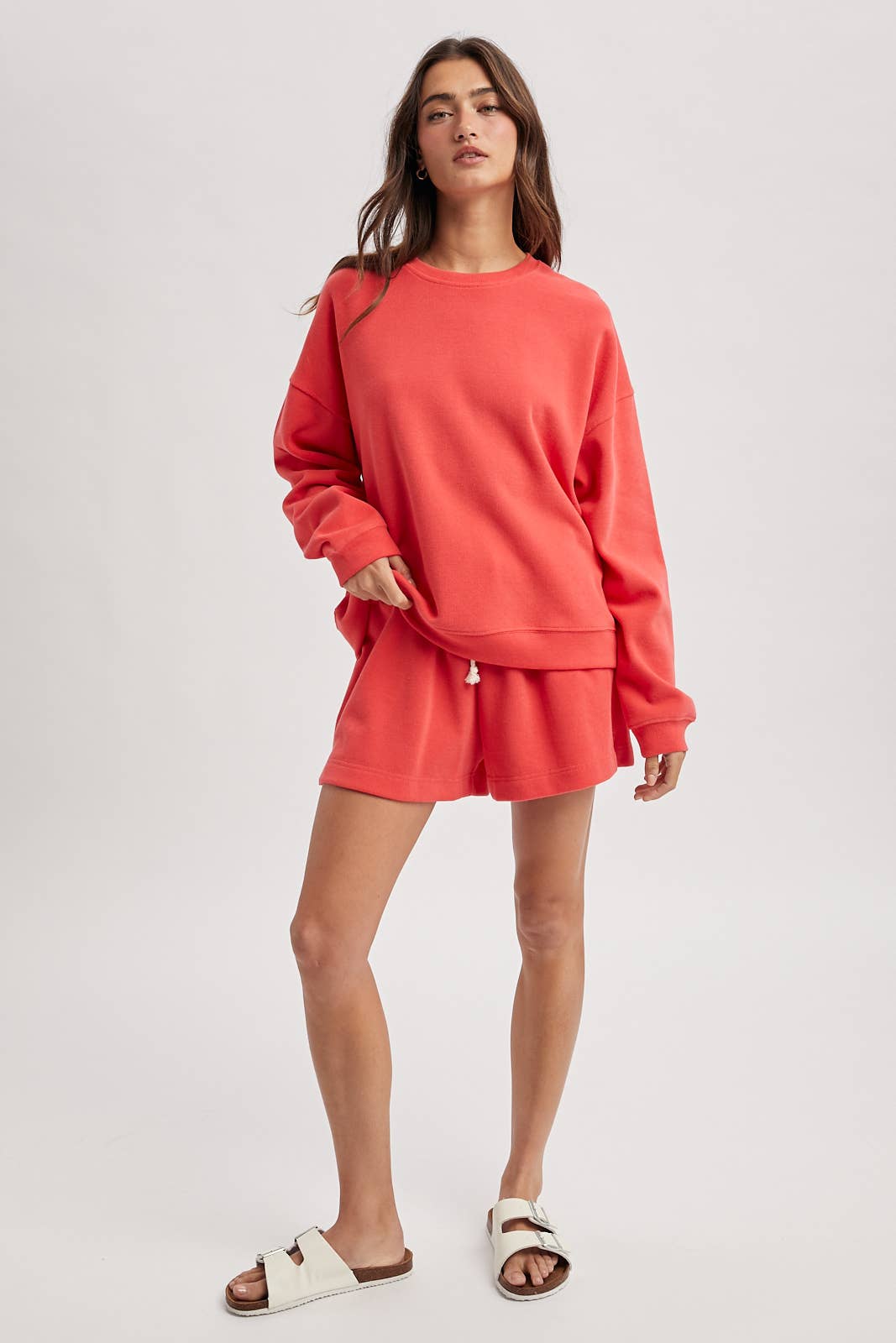 Woman wearing a coral sweatshirt and shorts set on a white background