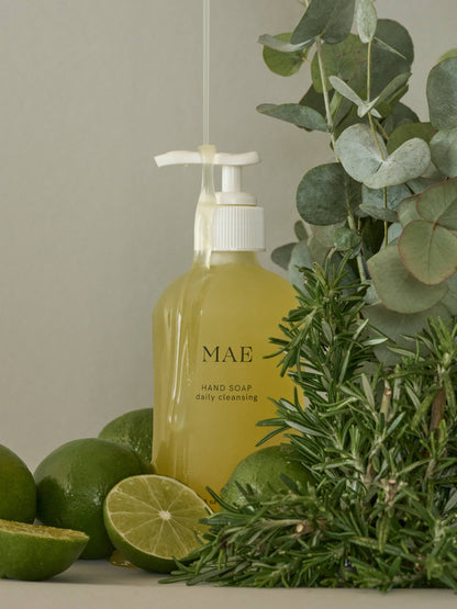Yellow hand soap bottle labeled 'MAE' with green limes and herbs on a neutral background