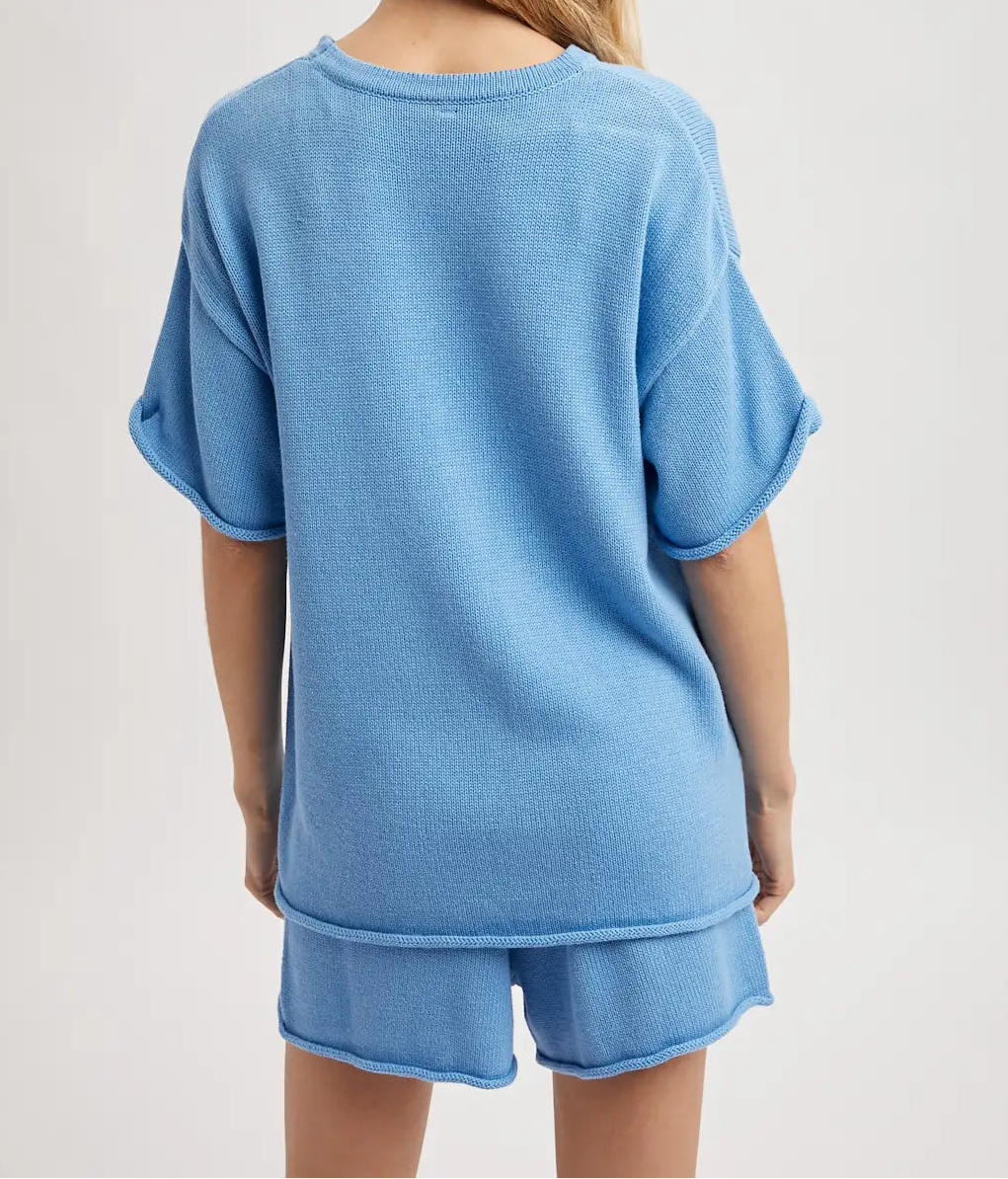 Person wearing a blue oversized t-shirt and shorts set on a light gray background