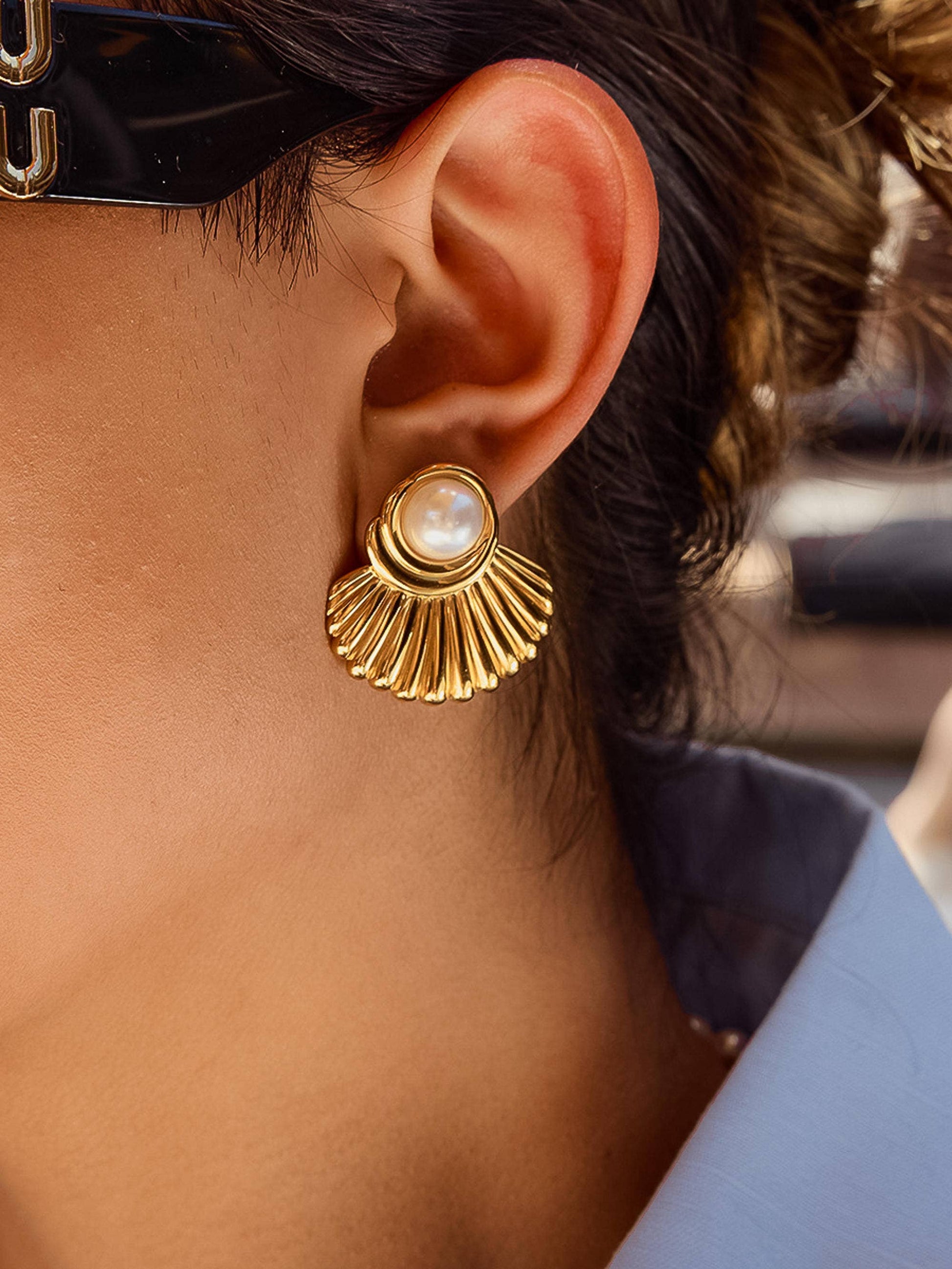 Close-up of a person wearing a gold earring with a pearl center.