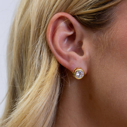 Close-up of a person wearing a gold earring with a clear gemstone.
