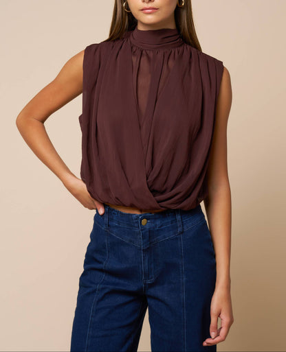 Woman wearing a brown sleeveless top and blue jeans against a beige background