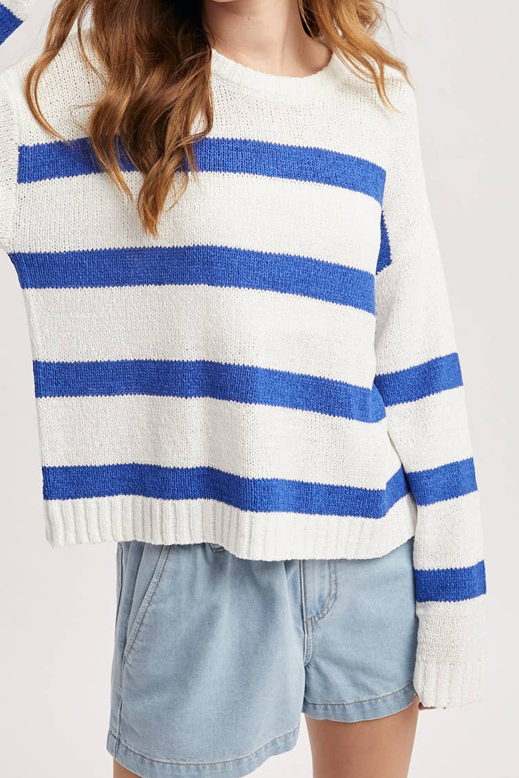 Woman wearing a blue and white striped sweater with light denim shorts on a plain background
