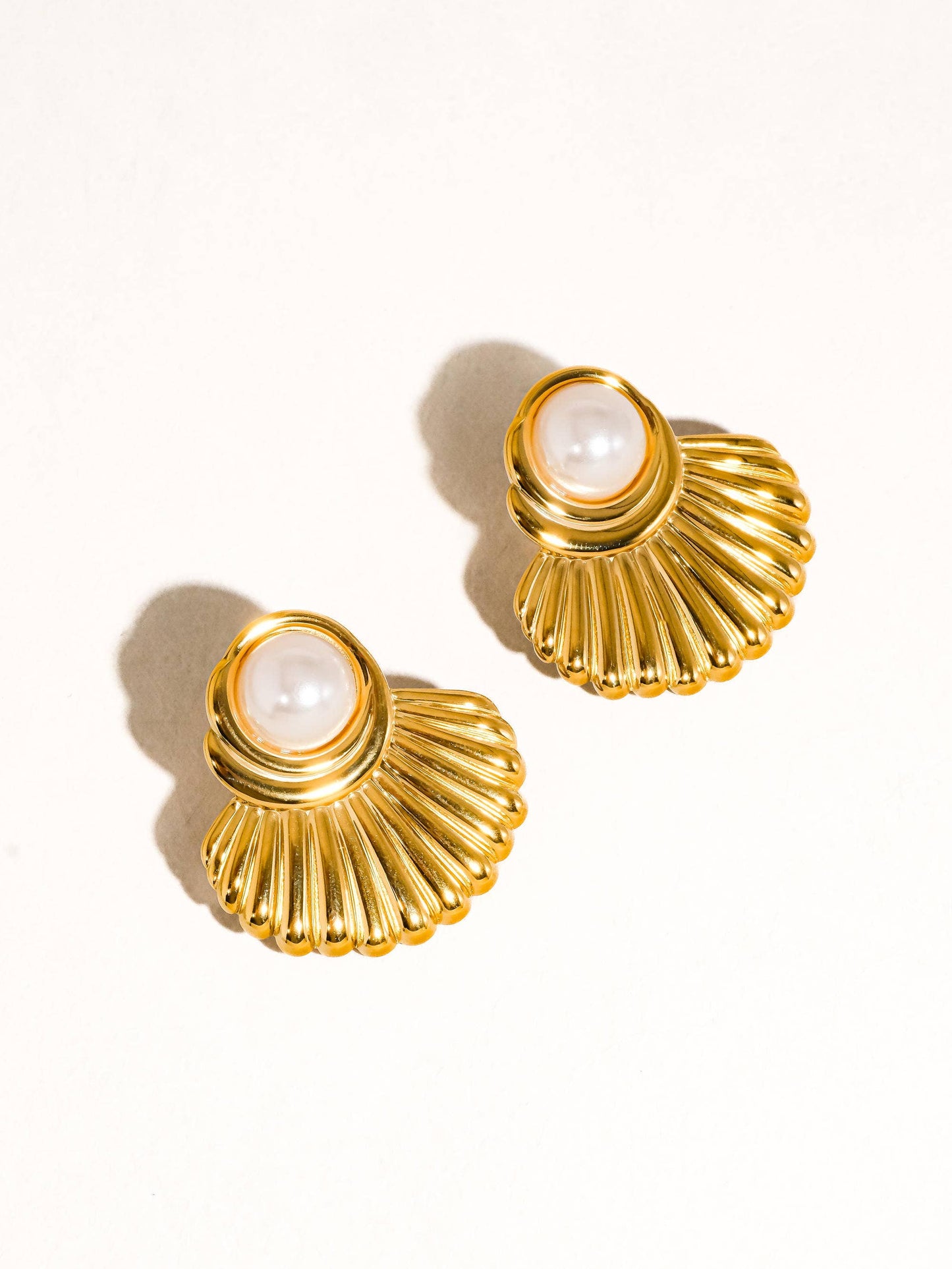Gold shell-shaped earrings with pearl centers on a white background