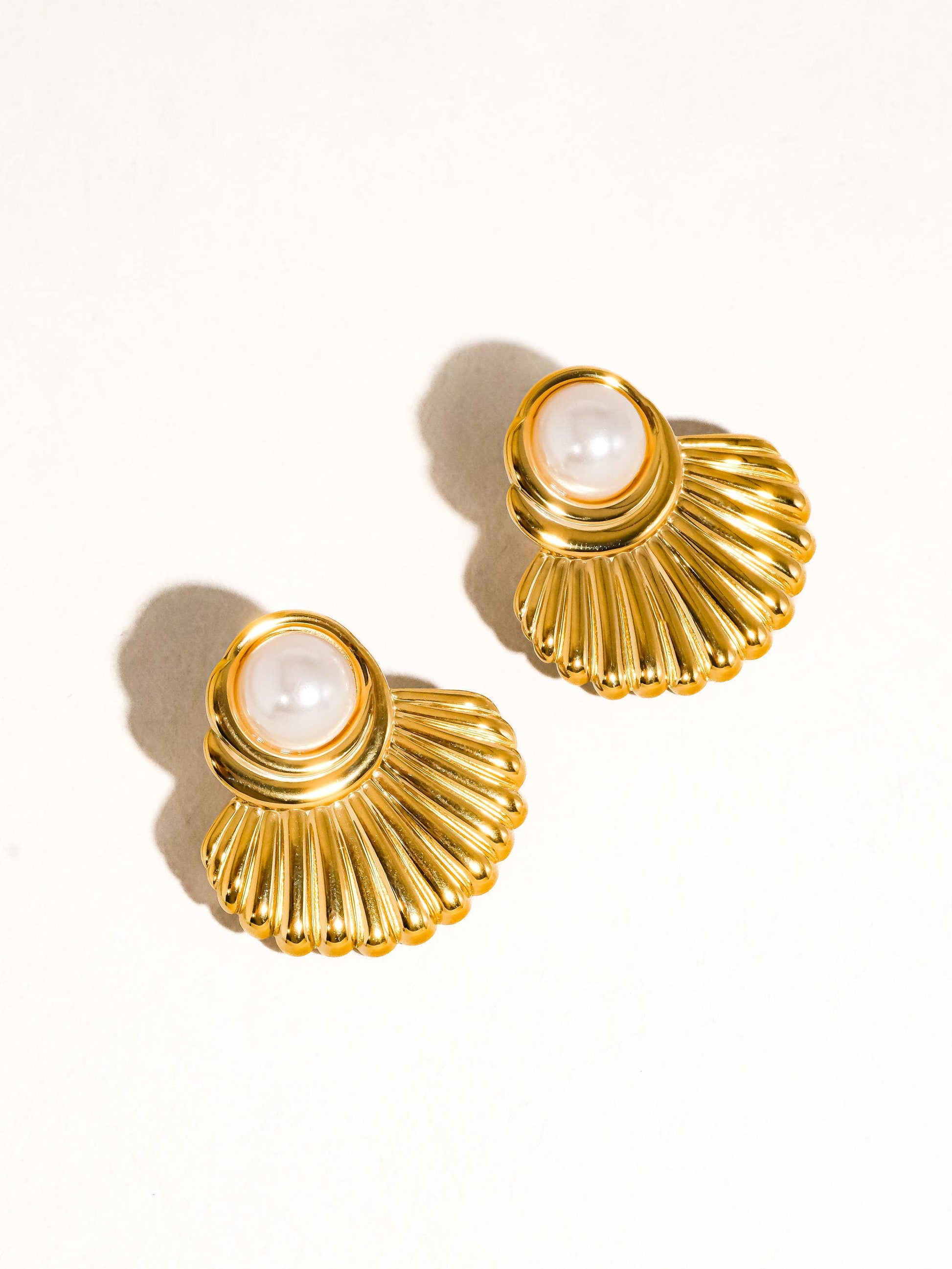 Gold shell-shaped earrings with pearl centers on a white background