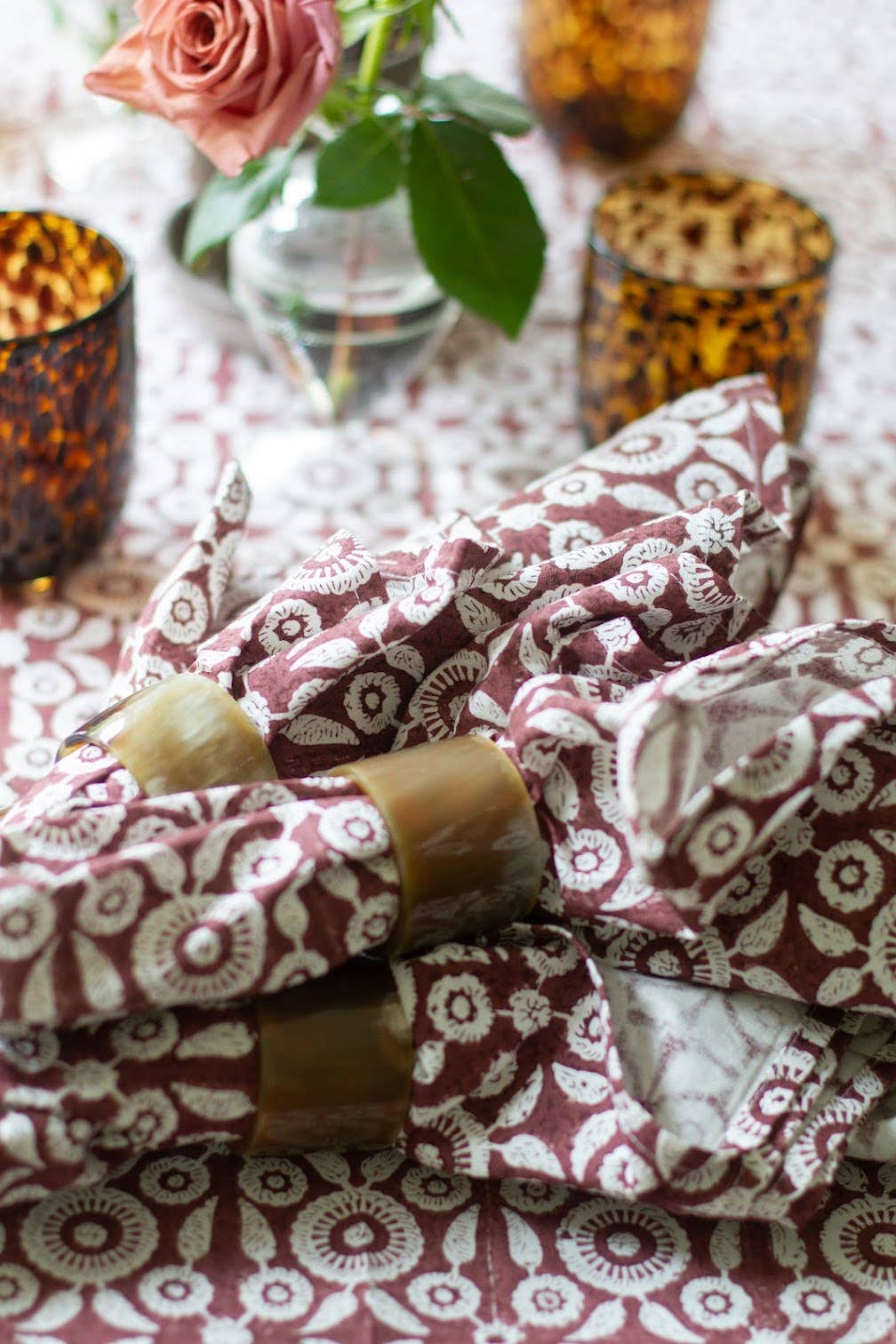 Patterned fabric wrapped around candles on a decorative table with flowers and candles.