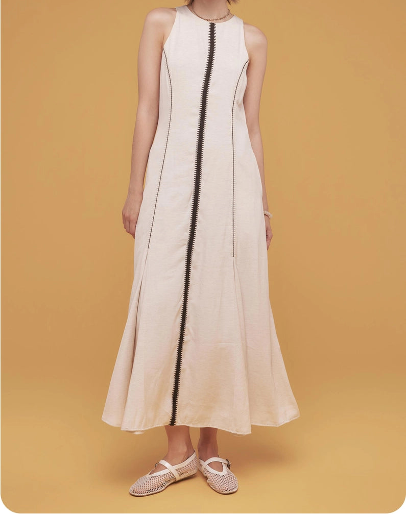 Woman wearing a white sleeveless dress with a black vertical stripe on a mustard yellow background