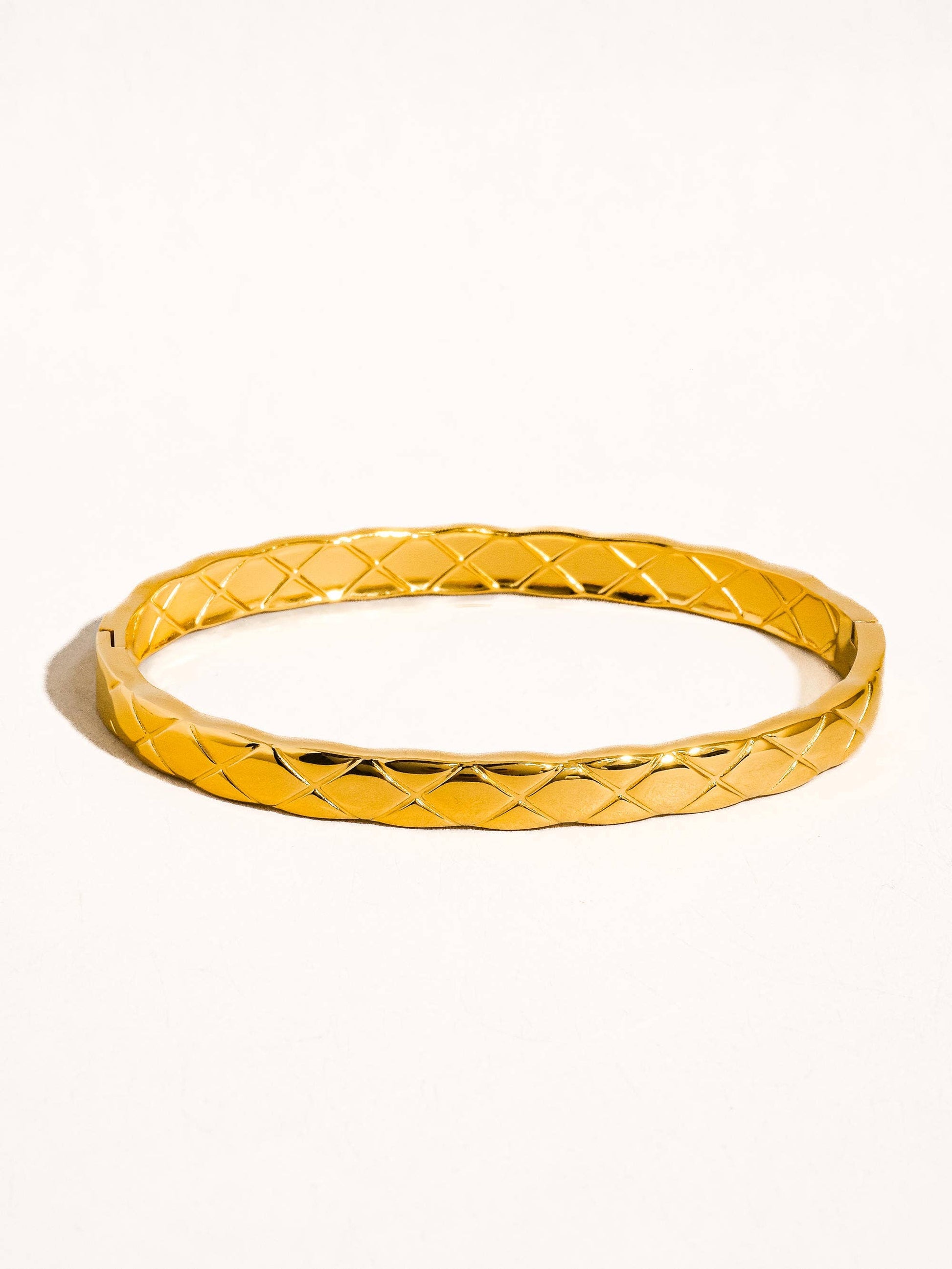 Gold bangle with textured pattern on a white background