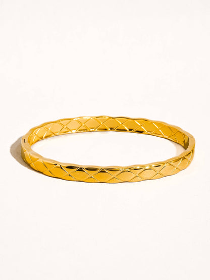 Gold bangle with textured pattern on a white background