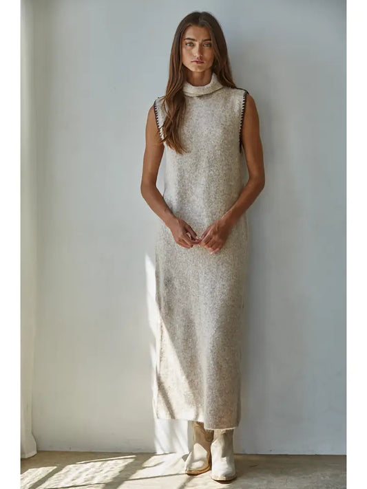 Woman wearing a long, light-colored dress against a plain wall.