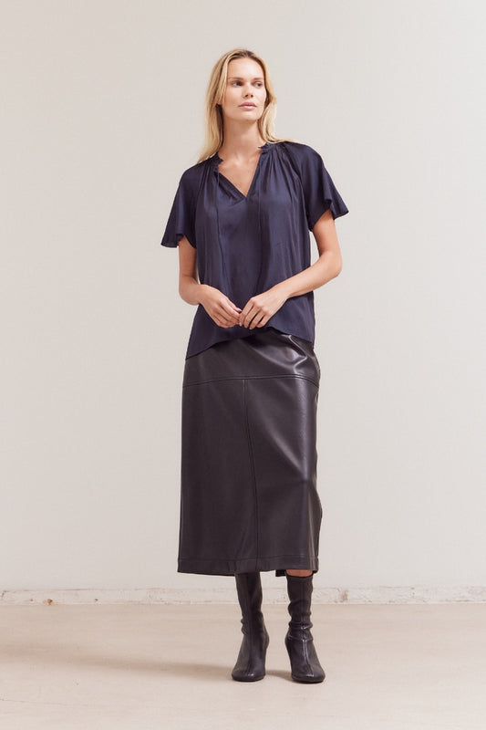 Woman wearing a dark blue top and black leather skirt against a plain background