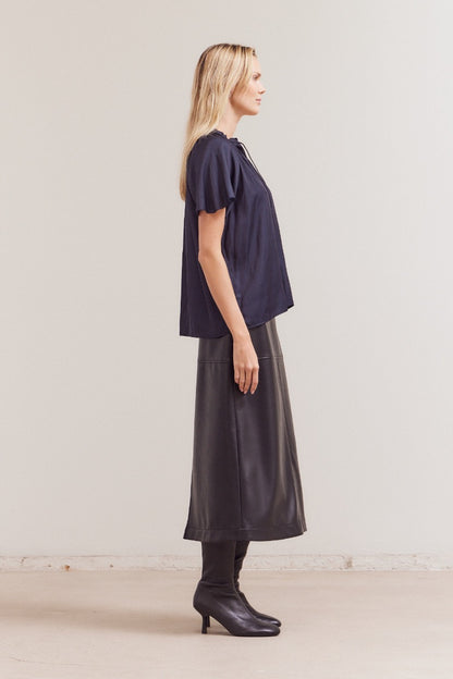 Woman wearing a dark blue top and black skirt against a plain background