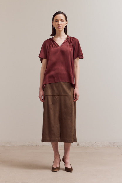 Woman wearing a rust-colored top and brown skirt against a plain background