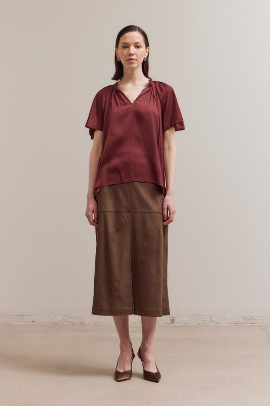 Woman wearing a rust-colored top and brown skirt against a plain background