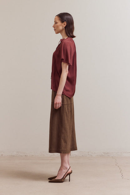 Woman wearing a burgundy top and brown skirt against a plain background