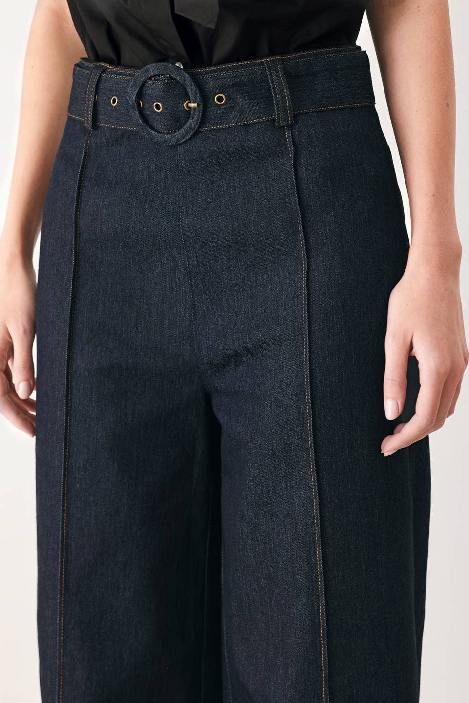 Close-up of a model wearing dark indigo wide-leg trousers with a matching dark belt and round metal buckle.