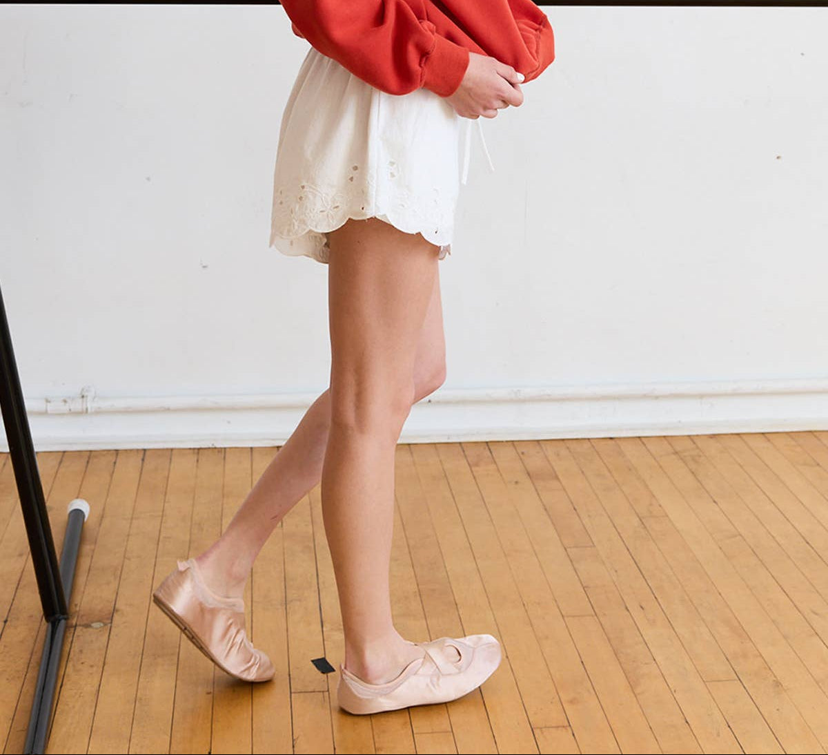 Woman in a red sweater and white skirt standing on a wooden floor.