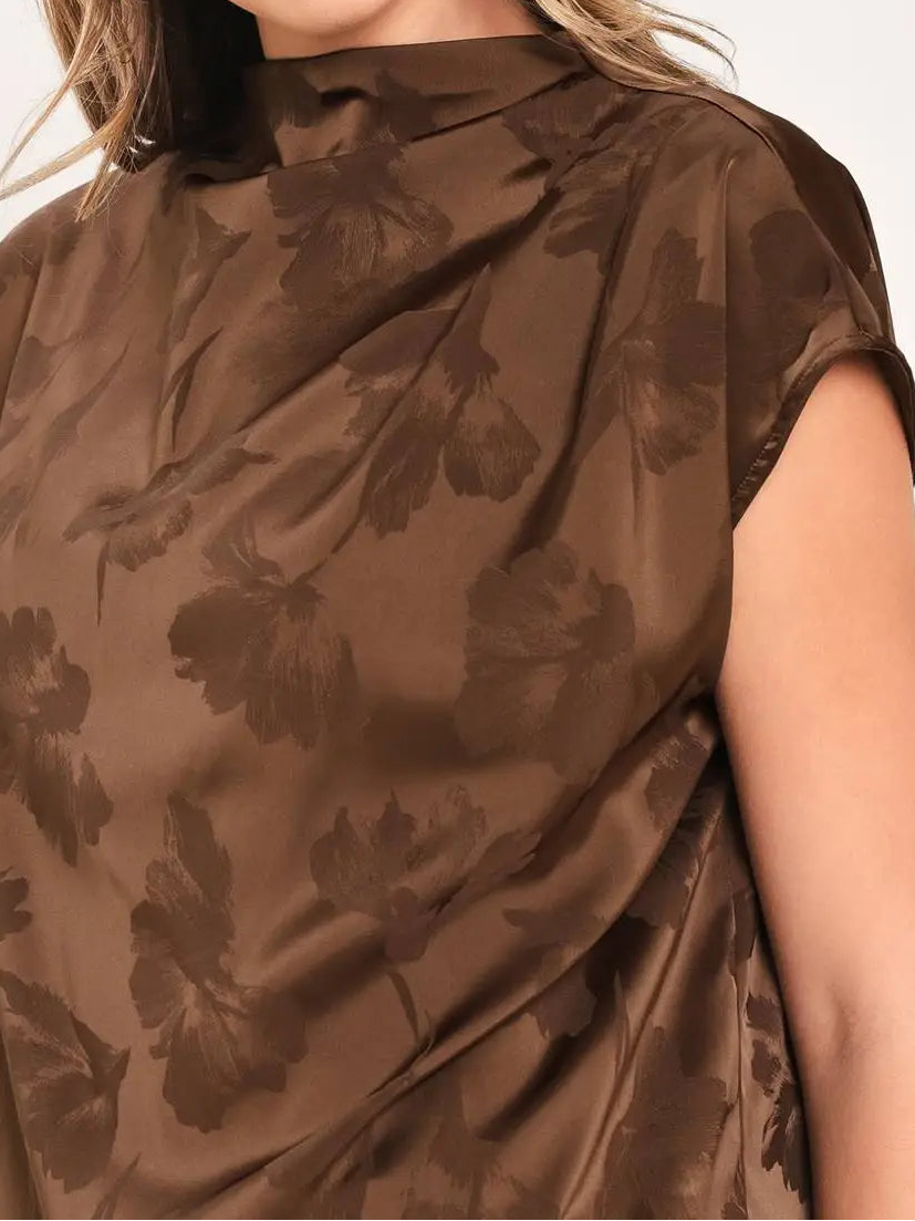 A woman wearing a brown satin-like top with a darker brown floral jacquard pattern, featuring a high mock neck and short sleeves.