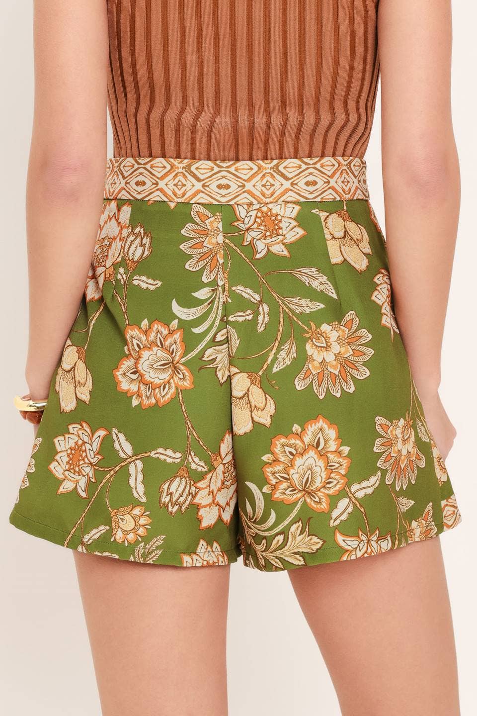 Woman wearing a brown sleeveless top and green floral skirt on a white background