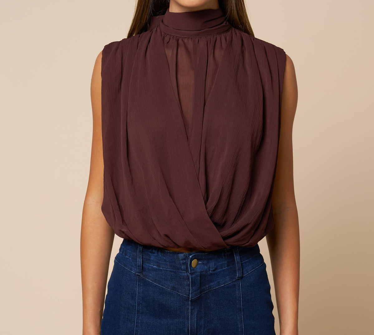 Woman wearing a brown sleeveless top and blue jeans against a beige background