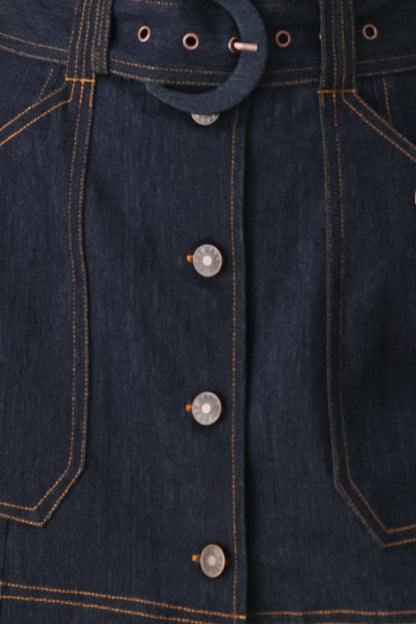 Close-up of a dark indigo denim garment showing the front button closure, belt loops, and contrast orange-yellow stitching.