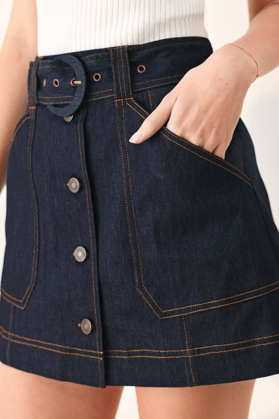 Dark denim skirt with button details worn by a person on a light background