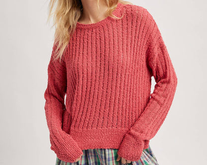 Woman wearing a pink chunky knit sweater and plaid skirt on a plain background