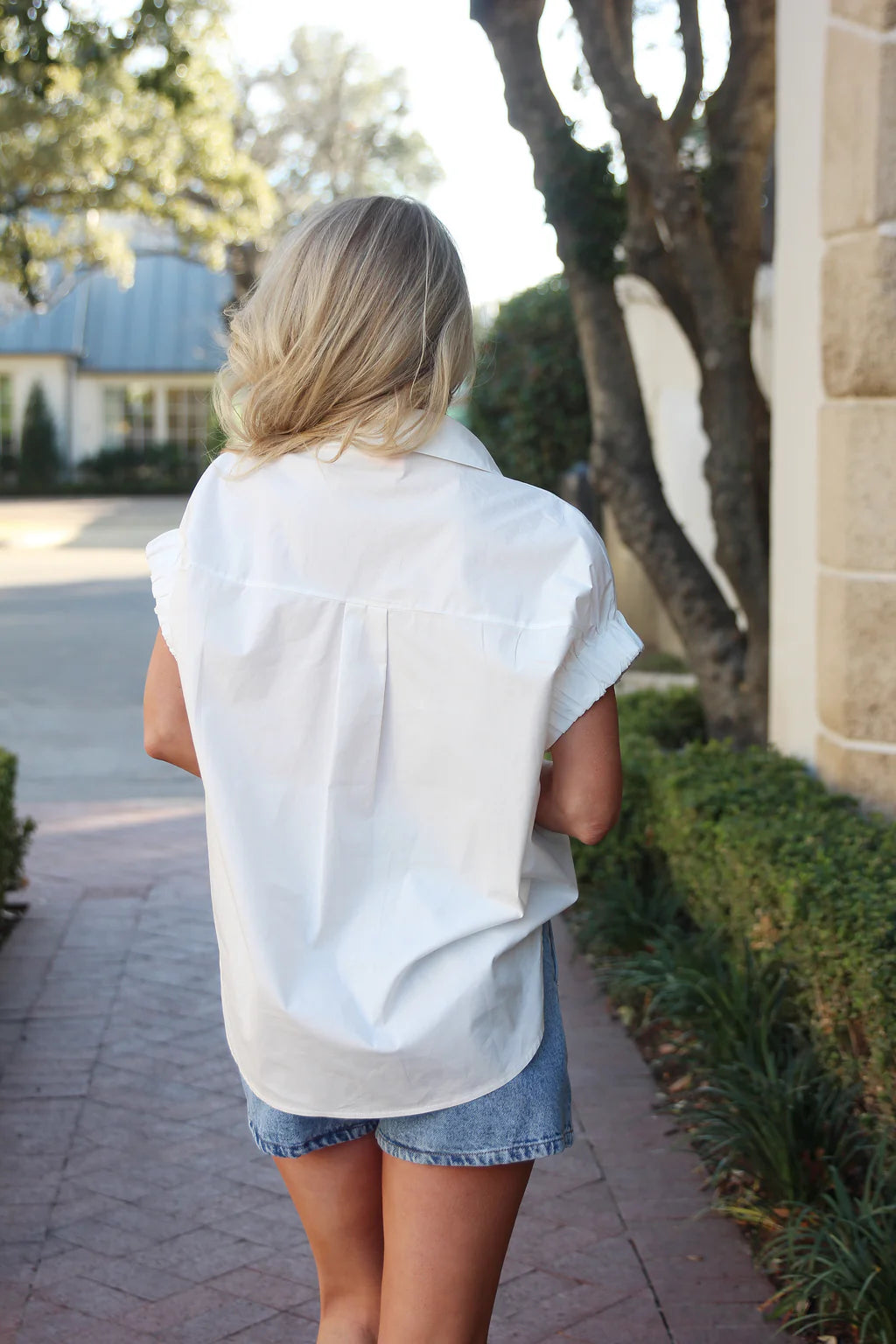 Woman wearing a white sleeveless shirt and denim shorts walking outdoors.