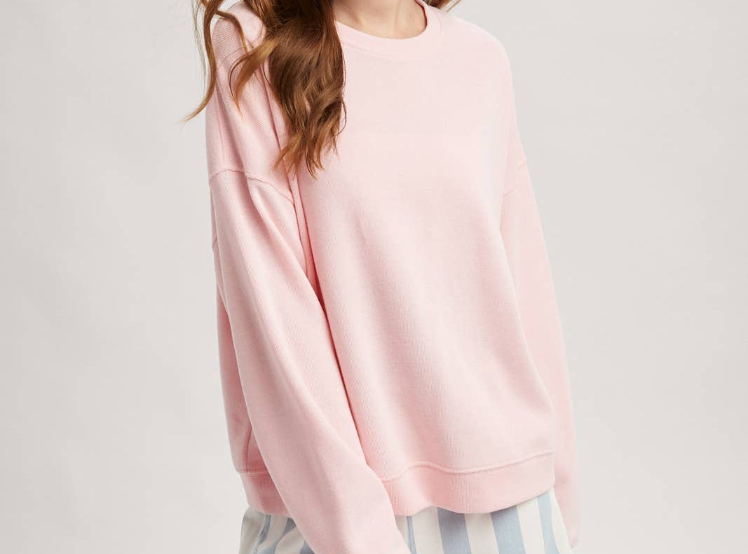 Woman wearing a pink sweatshirt and striped shorts on a light gray background