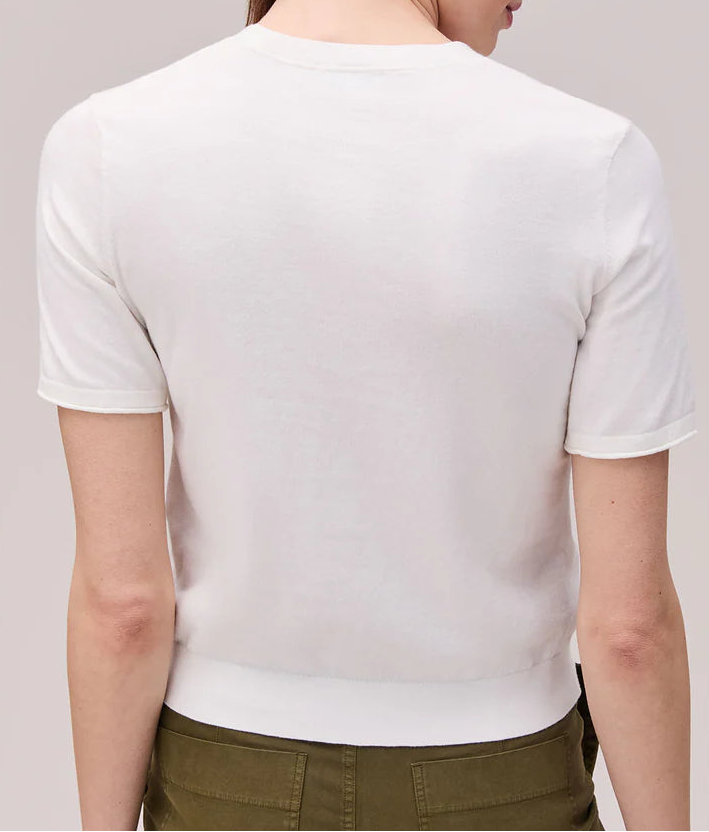 Woman wearing a white shirt and green pants against a plain background