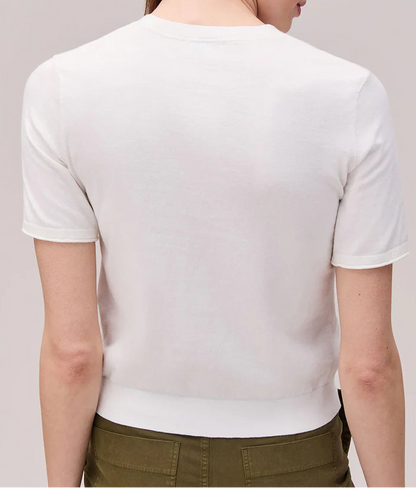 Woman wearing a white shirt and green pants against a plain background