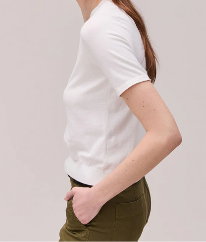 Woman wearing a white t-shirt and green pants against a plain background